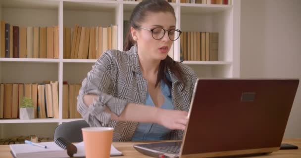 Closeup hajtás a fiatal sikeres kaukázusi üzletasszony a szemüveg segítségével a laptop a könyvtári irodában beltéri — Stock videók