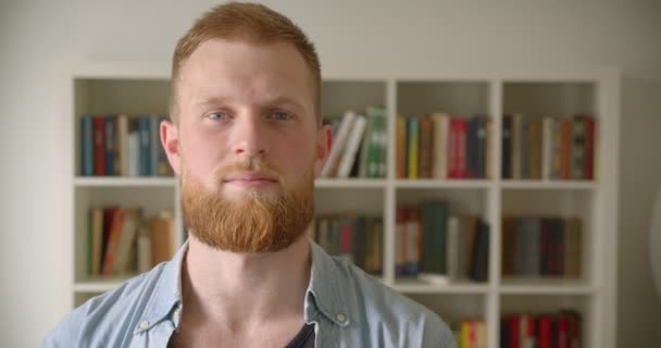 Primer plano retrato de pelirroja barbuda caucásica macho estudiante sonriendo felizmente mirando a la cámara en la biblioteca — Vídeo de stock