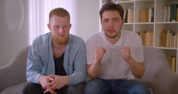 Närbild porträtt av två vuxna stilig kaukasiska män tittar på sport på TV och vara ledsen över förlorade sitt lag sitter på soffan inomhus — Stockvideo