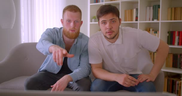 Close-up portret van twee volwassen knappe blanke mannen kijken naar voetbalspel op de TV en vieren gelukkig zittend op de Bank binnenshuis — Stockvideo