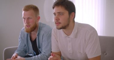 Tv'de spor izleyen iki yetişkin yakışıklı beyaz adamın kapalı koltukta otururken hayal kırıklığına uğrayan yakın çekim portresi