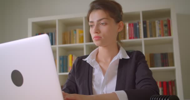 Nahaufnahme einer jungen hübschen kaukasischen Geschäftsfrau, die ihren Laptop benutzt und sich im Büro drinnen der Kamera zuwendet — Stockvideo