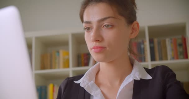 Nahaufnahme einer jungen hübschen kaukasischen Geschäftsfrau, die ihren Laptop benutzt und sich im Büro drinnen der Kamera zuwendet — Stockvideo
