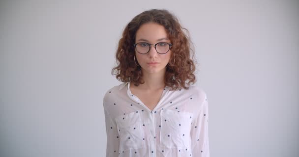 Κοντινό γύρισμα των νέων στυλάτο μακριά μαλλιά σγουρά Καυκάσιος θηλυκό σε γυαλιά χαμογελώντας χαρούμενη κοιτάζοντας την κάμερα με φόντο απομονώνεται σε λευκό — Αρχείο Βίντεο