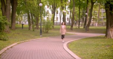 Parkta açık havada kameraya doğru mutlu bir şekilde yürüyen genç uzun saçlı kıvırcık beyaz beyaz kadın Closeup ateş