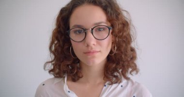 Genç sevimli uzun saçlı kıvırcık kafkas kadın yakından gülümseyen mutlu beyaz izole arka plan ile kameraya bakarak gözlüklerini sabitleme