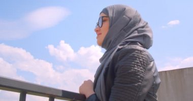 Türbanlı genç güzel müslüman kadın ve gözlük şehir şehir görünümüne bakarak ve neşeyle gülümseyerek kameraya dönüyor closeup ateş