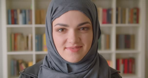 Primo piano ritratto di giovane studentessa musulmana attraente in hijab sorridente felicemente guardando la fotocamera nella biblioteca del college al chiuso — Video Stock