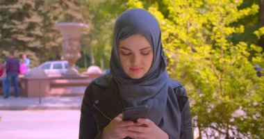 Hijab genç güzel müslüman kadın closeup ateş kamera şehir açık havada mutlu gülümseyerek bakarak telefon kullanarak