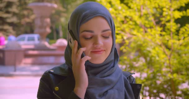 Κοντινό γύρισμα της νεαρής όμορφη μουσουλμανική θηλυκό σε μαντίλα μιλώντας στο τηλέφωνο χαμογελώντας ευτυχισμένα στην αστική πόλη σε εξωτερικούς χώρους — Αρχείο Βίντεο