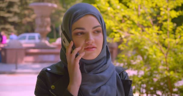 Closeup shoot of young pretty muslim female in hijab talking on the phone smiling happily on the street in the urban city outdoors — Stock Video