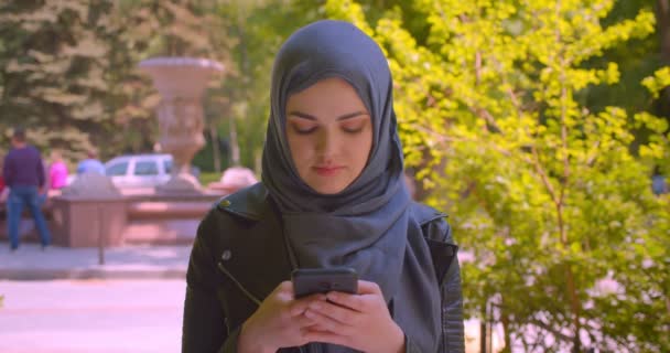 Zavácení mladé krásné muslimské ženy v hidžábu s použitím telefonu, který se šťastně usmívá v městském městě — Stock video