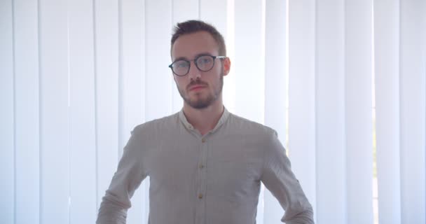 Closeup portrait of young handsome caucasian businessman looking at camera with arms in his pockets in the white apartment — Stock Video