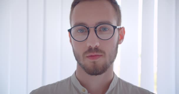 Κοντινό πλάνο από νέους όμορφους Καυκάσιους επιχειρηματίες πρόσωπο σε γυαλιά κοιτάζοντας την κάμερα στο λευκό διαμέρισμα — Αρχείο Βίντεο