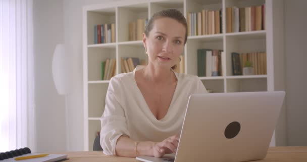 Close-up retrato de idosos caucasiano morena empresária usando o laptop olhando para a câmera sorrindo alegremente no escritório dentro de casa — Vídeo de Stock