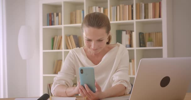 Close-up portret van oudere Kaukasische brunette zakenvrouw het gebruik van de laptop en het nemen van selfies op de telefoon in het kantoor binnenshuis — Stockvideo