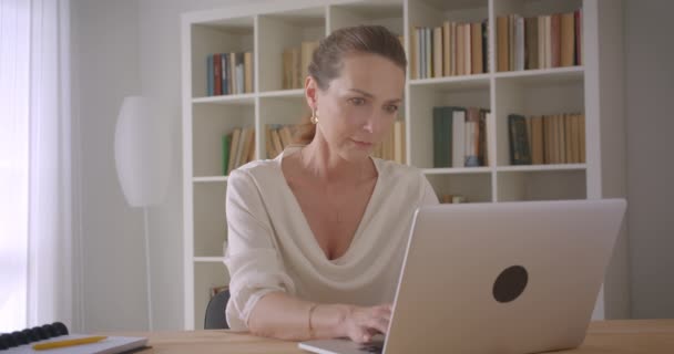 Close-up portret van oudere Kaukasische brunette zakenvrouw met behulp van de laptop op zoek naar camera in het kantoor binnenshuis — Stockvideo