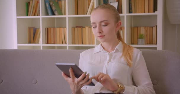 Primer plano retrato de joven bastante caucásica rubia estudiante utilizando la tableta y mostrando la pantalla verde a la cámara sentado en el sofá interior en el apartamento — Vídeo de stock