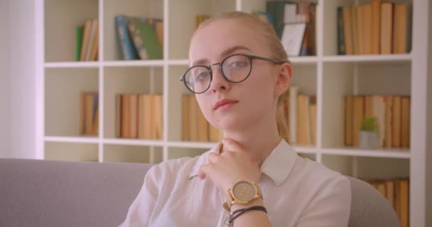 Closeup retrato de jovem muito caucasiano loira estudante em óculos posando na frente da câmera sentada no sofá dentro de casa no apartamento — Vídeo de Stock