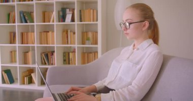 Dolap yan görünüm genç güzel beyaz sarışın iş kadının ın portresi gözlüklü dizüstü bilgisayar kullanarak dairenin içinde kanepede oturan kameraya bakarak