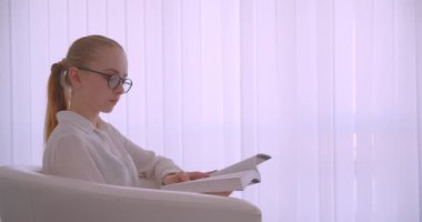 Beyaz dairede kapalı koltukta oturan kameraya bakan bir kitap okuyan gözlükgenç güzel beyaz sarışın iş kadını Closeup yan görünümü