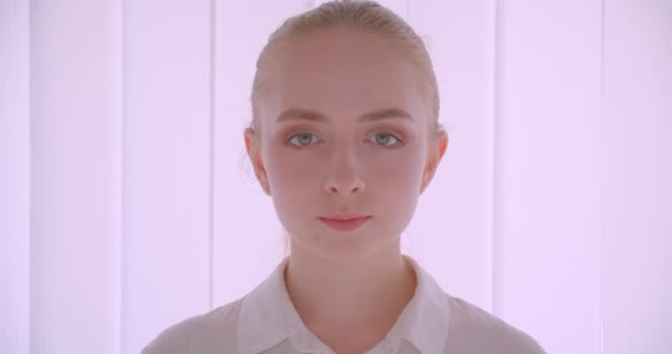 Gros plan portrait de jeune jolie caucasienne blonde visage féminin regardant la caméra avec une expression souriante à l'intérieur dans l'appartement blanc — Video