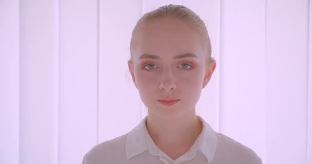 Gros plan portrait de jeune jolie caucasienne blonde visage féminin regardant la caméra avec sourire expression joyeuse à l'intérieur dans l'appartement blanc — Video