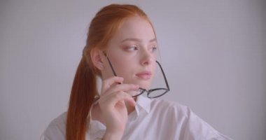 Beyaz bir odada koltukta neşeyle oturan gülümseyerek gözlüklerini koyarak kameraya bakan genç sevimli kafkas kızıl saçlı kadın Closeup portre