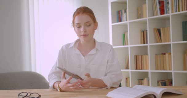 Närbild porträtt av unga ganska rödhårig kvinnlig student använder tabletten och visar grön Chroma skärm till kameran sitter vid skrivbordet i en mysig lägenhet — Stockvideo