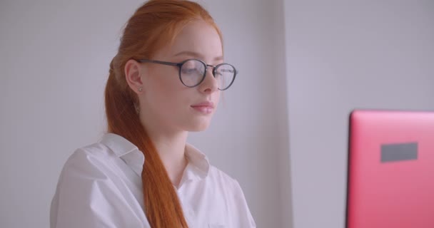 Nahaufnahme Porträt einer jungen netten kaukasischen rothaarigen Geschäftsfrau mit Brille, die den Laptop benutzt und in die Kamera lächelt, glücklich im Sessel im Büro sitzend — Stockvideo
