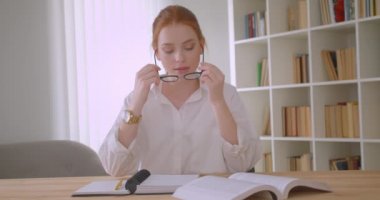 Tablet kullanarak ve rahat bir dairede masada oturan bir dizüstü bilgisayar yazma at kuyruklu gözlük genç sevimli kızıl saçlı kız öğrencinin Closeup portre