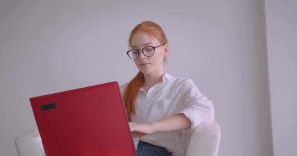 Beyaz bir odada koltukta oturan dizüstü bilgisayar kullanarak gözlük genç güzel beyaz kızıl saçlı iş kadının Closeup portre
