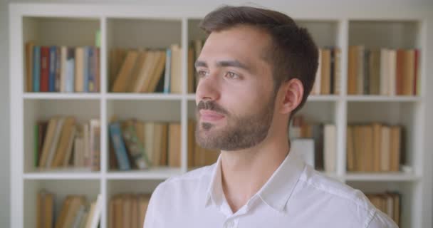 Close-up retrato de adulto bonito caucasiano homem olhando para câmera sorrindo alegremente na biblioteca dentro de casa — Vídeo de Stock