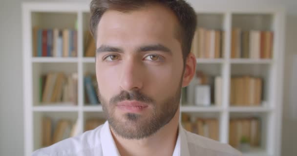 Gros plan portrait d'adulte beau barbu caucasien homme tournant et regardant caméra dans la bibliothèque avec des étagères sur le fond à l'intérieur — Video