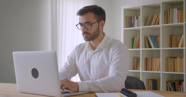 Zbliżenie portret dorosłego przystojny kaukaski biznesmen za pomocą laptopa i patrząc na kamerę w biurze w pomieszczeniu — Wideo stockowe