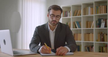 Gözlük içinde yetişkin yakışıklı beyaz işadamı ofis kapalı evde mutlu gülümseyen kamera bakarak not alma laptop kullanarak portre