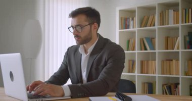 Ofis kapalı not alma dizüstü bilgisayar kullanarak gözlüklü yetişkin yakışıklı beyaz işadamı portre kapatmak