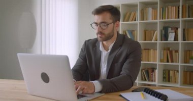 Ofiste iç mekanlarda düşünceli olan dizüstü bilgisayarı gözlüklü yetişkin yakışıklı beyaz işadamının yakın çekim portresi