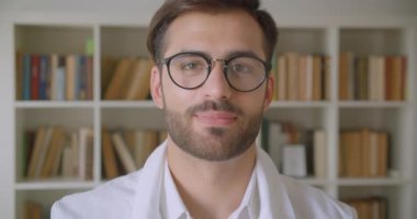 Gözlüklü yetişkin yakışıklı beyaz işadamının kapalı arka planda kitaplıklar ile kütüphanede kameraya bakan closeup portre