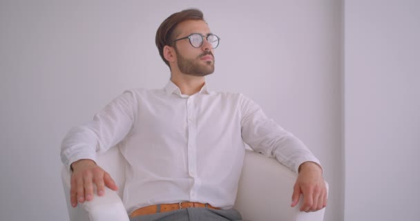 Nahaufnahme Portrait von erwachsenen schönen bärtigen kaukasischen Geschäftsmann sitzt im Sessel im weißen Büro drinnen — Stockvideo