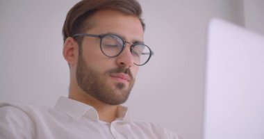 Kapalı beyaz ofiste koltukta oturan dizüstü bilgisayar kullanarak gözlük yakışıklı sakallı kafkas işadamıcloseup portre