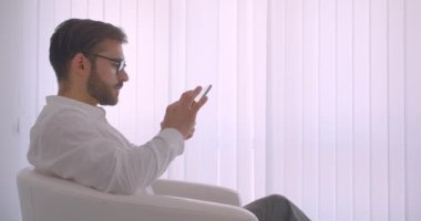 Kapalı beyaz ofiste koltukta oturan tablet kullanarak gözlük yetişkin yakışıklı sakallı kafkas işadamıcloseup yan görünüm portresi