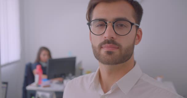 Primer plano retrato de guapo exitoso hombre de negocios caucásico en gafas mirando a la cámara en la oficina blanca en el interior con empleado en el fondo — Vídeos de Stock