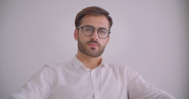 Nahaufnahme Porträt eines erwachsenen gutaussehenden bärtigen kaukasischen Geschäftsmannes mit Brille, der glücklich lächelnd in die Kamera blickt und im Sessel im weißen Büro drinnen sitzt — Stockvideo
