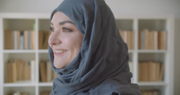Closeup portré fiatal muzulmán vonzó üzletasszony a hidzsáb nézi kamera mosolygós boldogan a könyvtárban beltéri — Stock videók