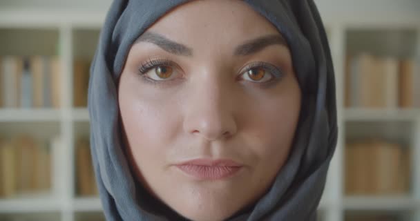 Κοντινό πλάνο της νεαρής Αραβικής ελκυστικής επιχειρηματία στην χιτζάμπ κοιτάζοντας την κάμερα στη βιβλιοθήκη σε εσωτερικούς χώρους — Αρχείο Βίντεο