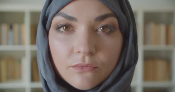 Κοντινό πλάνο της νεαρής Αραβικής ελκυστικής επιχειρηματία στη μαντίλα κοιτάζοντας την κάμερα χαμογελώντας χαρούμενα στη βιβλιοθήκη σε εσωτερικούς χώρους — Αρχείο Βίντεο