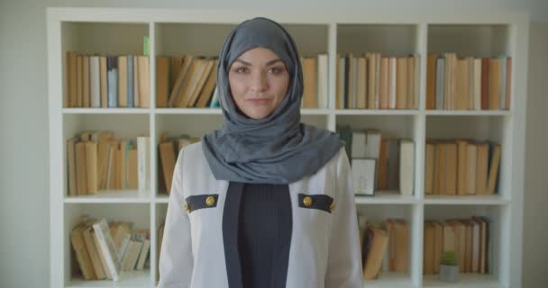 Closeup portrait of young muslim attractive female doctor in hijab looking at camera in the library indoors — Stock Video