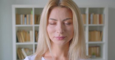 Arka planda kütüphaneler ile kütüphanede neşeli kapalı gülümseyen kamera bakarak yetişkin beyaz sarışın kadın yakın çekim portre