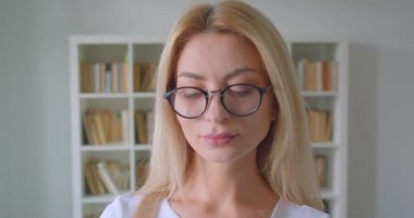 Kamerada gözlüklü yetişkin beyaz sarışın kadın fotoğraf makinesi görünümlü mutlu kapalı kütüphanede gülümseyen